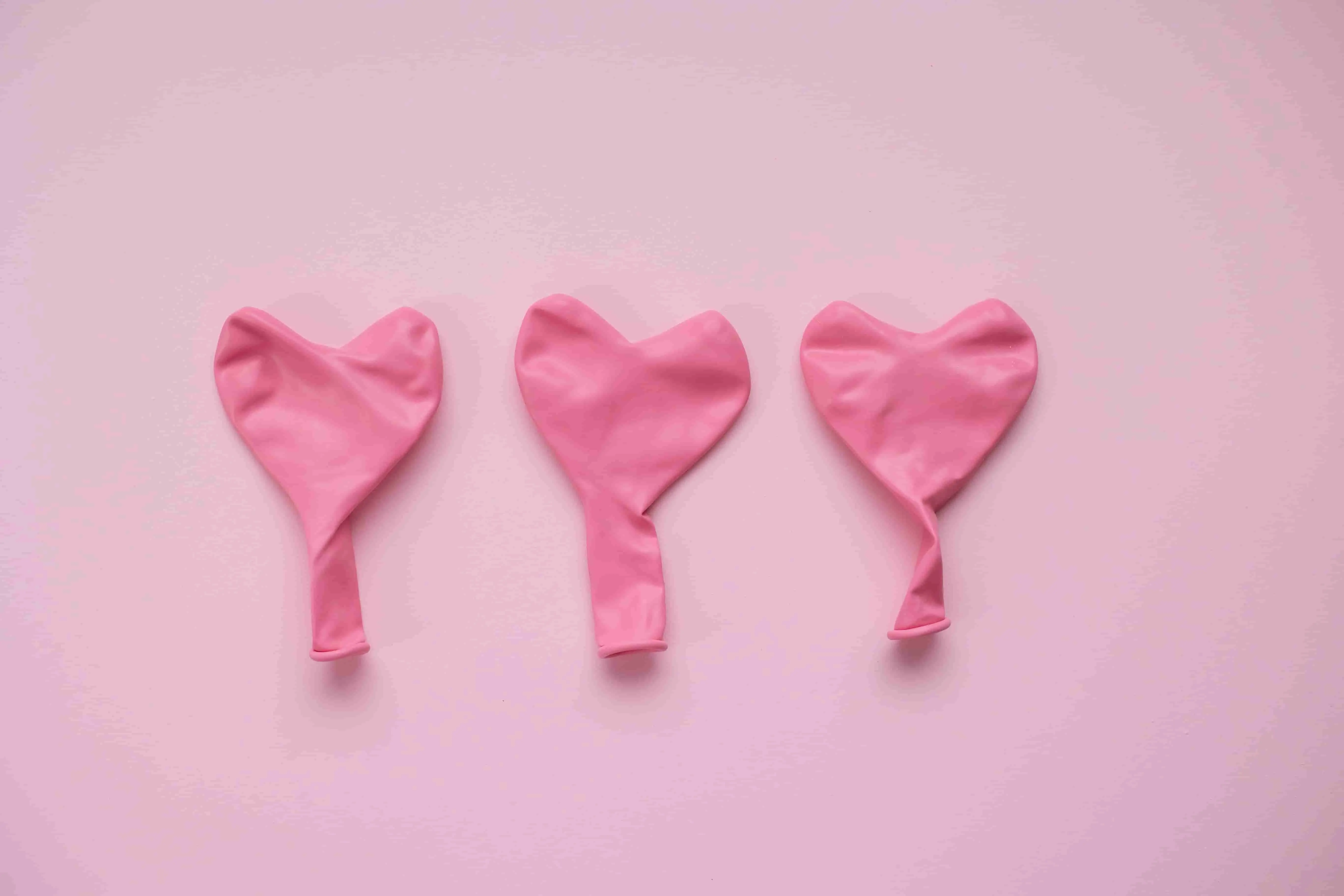 Image of 3 deflated pink balloons against a light pink background